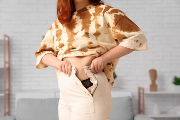 Image of woman trying to do her trousers up after pregnancy weight gain Southsea